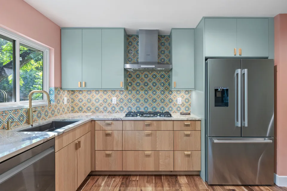 Corner of white oak cabinets with a stainless refrigerator, range hood and patterned tile