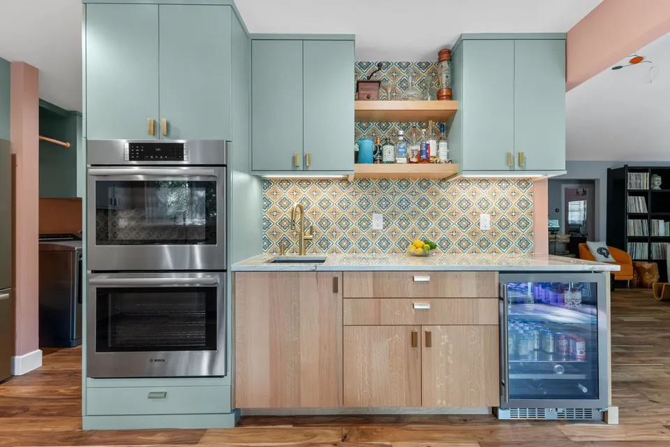 Double wall ovens in sage cabinets beside patterned tile, open shelves and a beverage fridge