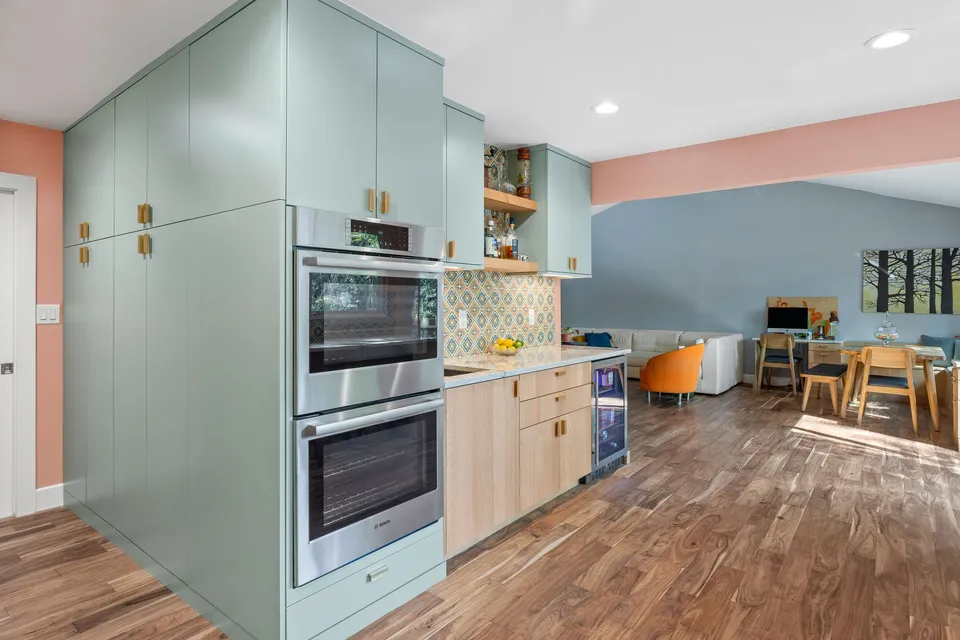 Floor-to-ceiling sage cabinets with double ovens, open to the dining and living area
