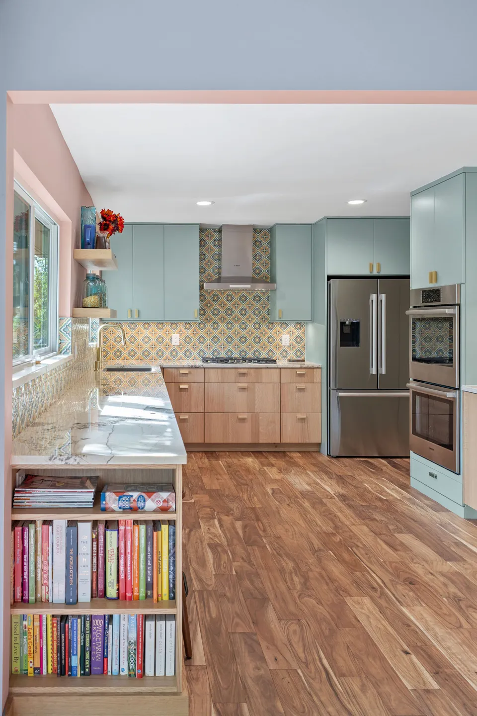 Kitchen seen past a bookshelf peninsula, with sage uppers and a stainless refrigerator