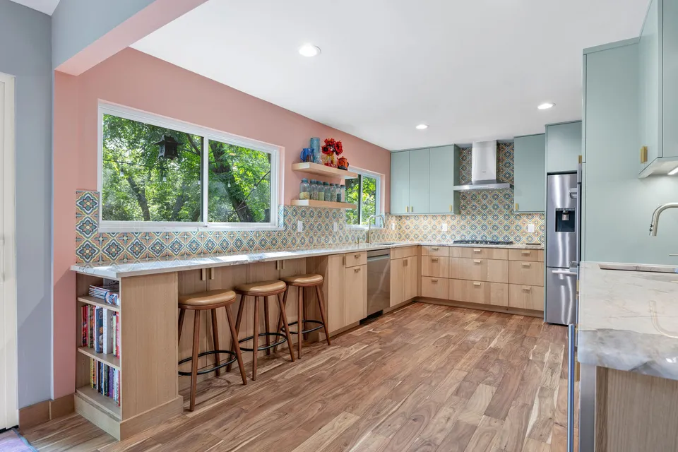 Kitchen with pink walls, a peninsula with bar stools and sage upper cabinets