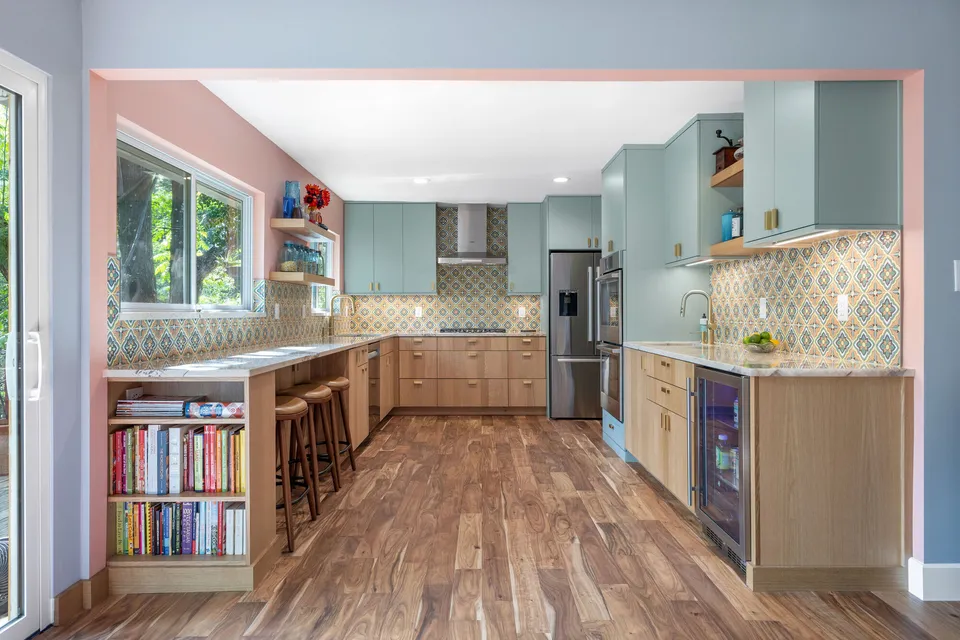Long view of the kitchen with white oak lower cabinets, sage uppers and a bookshelf