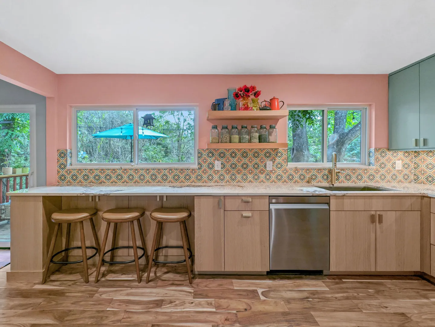Peninsula with three bar stools, a dishwasher and open shelves below two windows