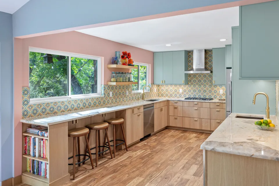 Peninsula with wood bar stools, a bookshelf and patterned tile below pink walls