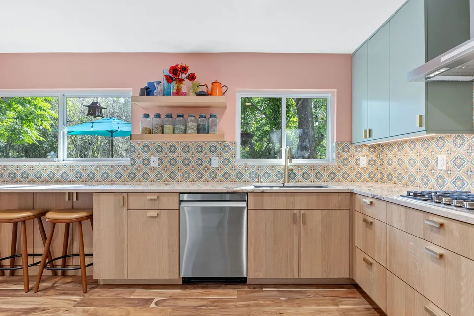 Sink wall with white oak cabinets, a dishwasher and open shelves between two windows