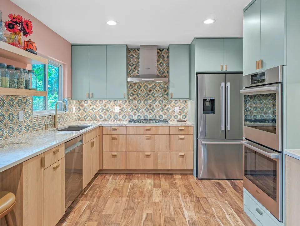 Stainless refrigerator and double ovens in sage cabinets with pink walls and patterned tile