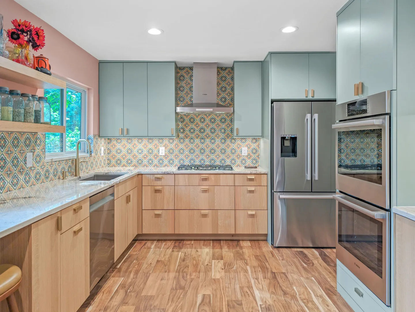 Stainless refrigerator and double ovens in sage cabinets with pink walls and patterned tile