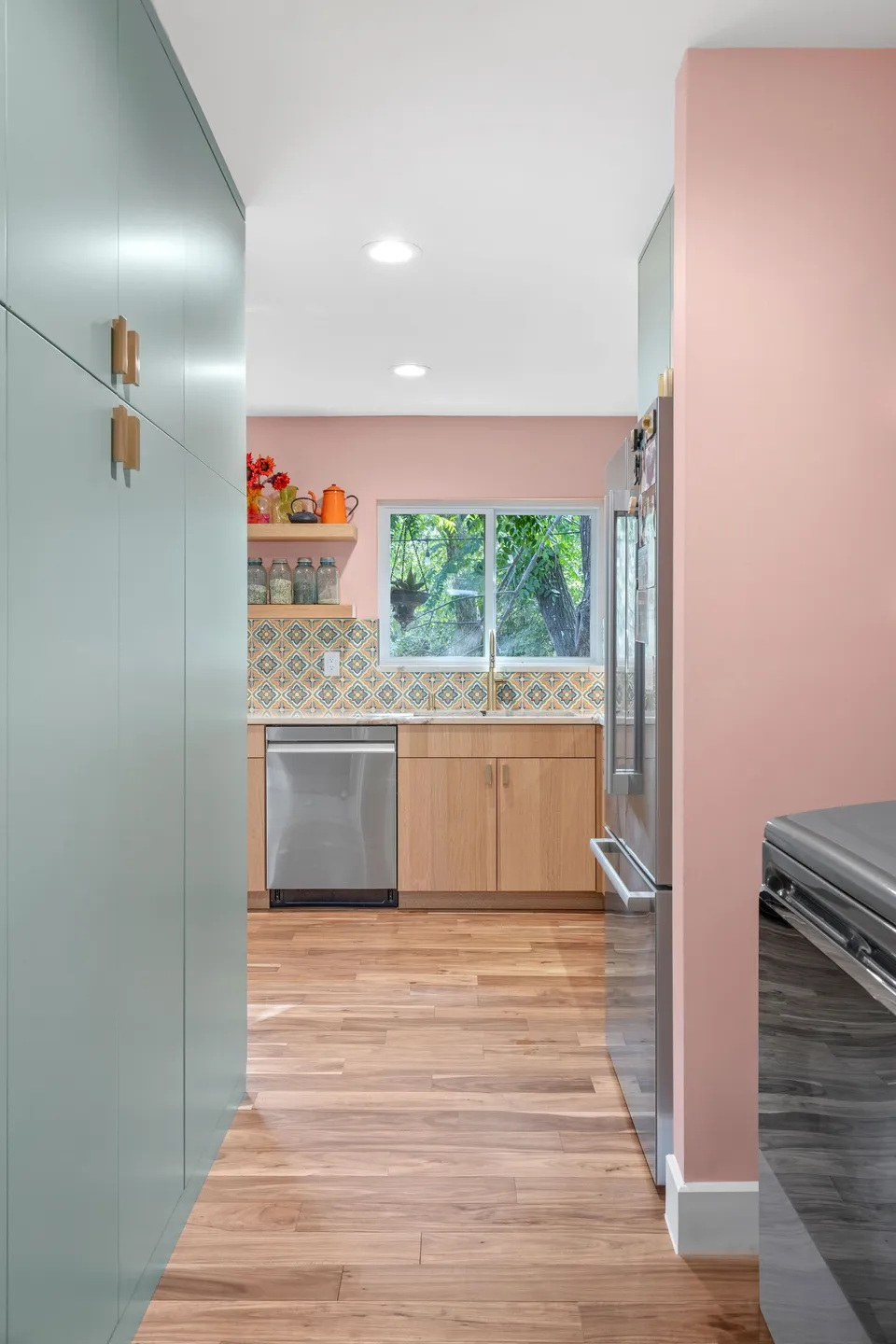 Kitchen after the remodel, with tall sage green cabinets, pink walls and white oak lower cabinets