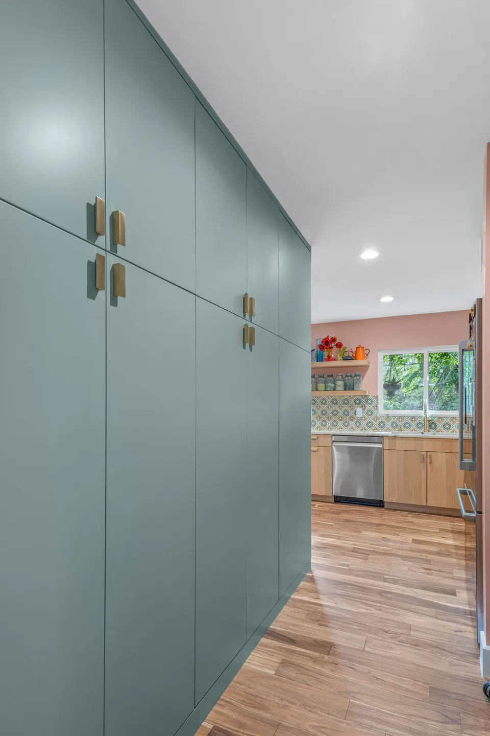 Wall of tall sage green pantry cabinets with brass pulls