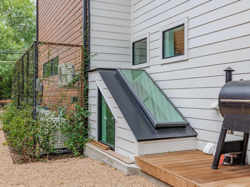 Angled glass skylight over the basement beside a wood step and a grill