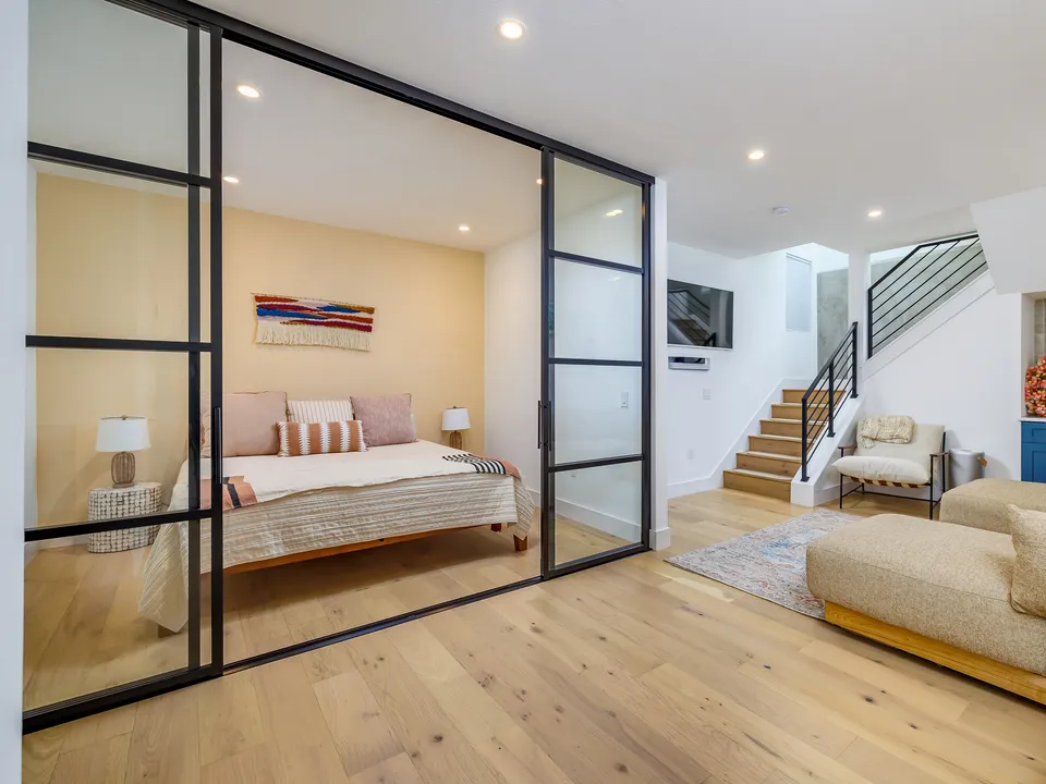 Basement guest bedroom behind black steel-framed glass doors