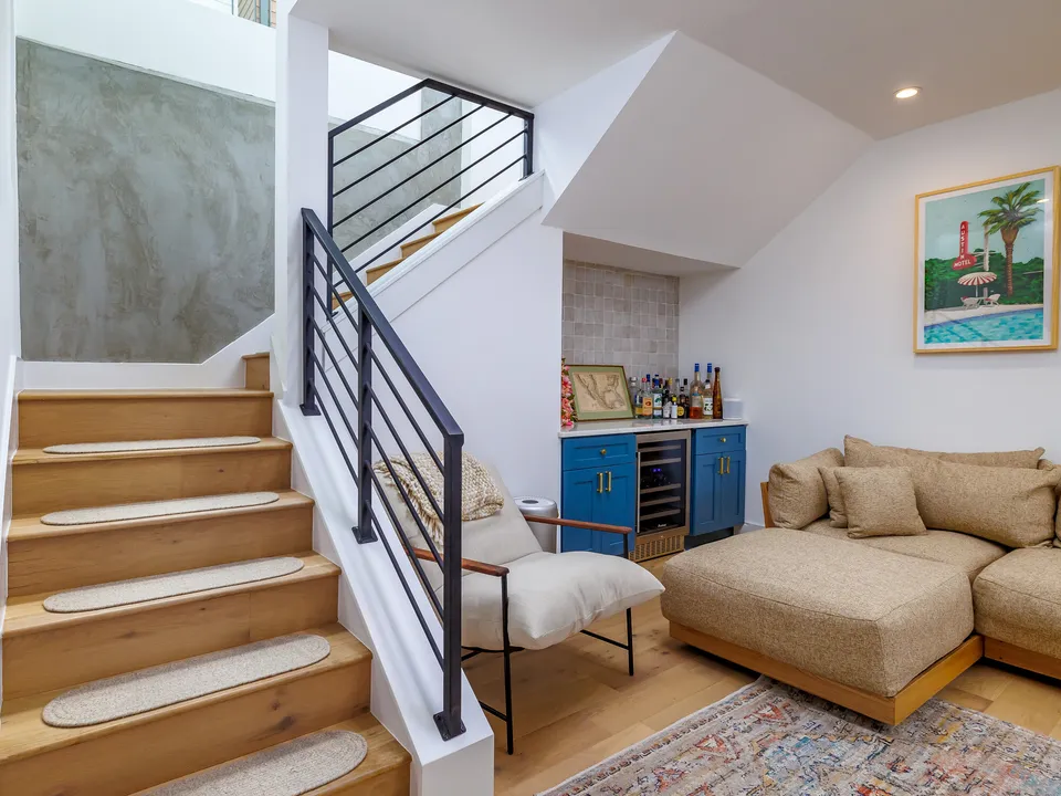 Basement living area with a new oak stair, black railing and a blue bar cabinet