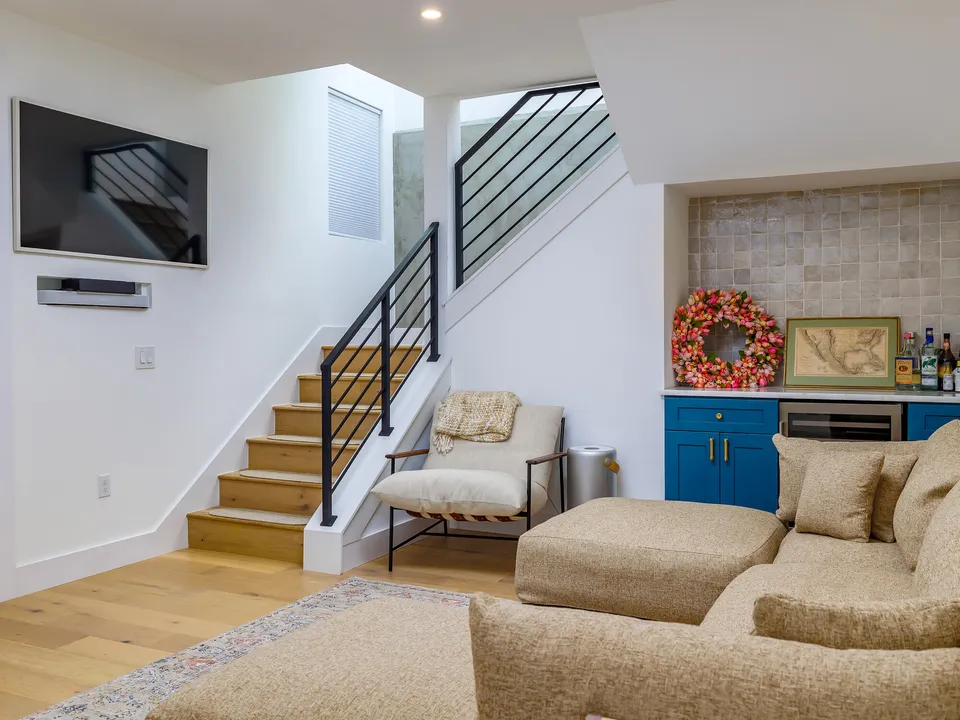 Basement lounge with a sectional, a TV and a bar with blue cabinets