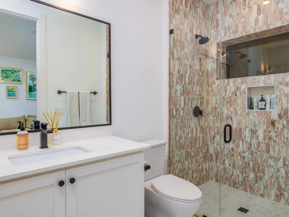 Bathroom after the remodel, with pebble-pattern shower tile and a black-framed mirror