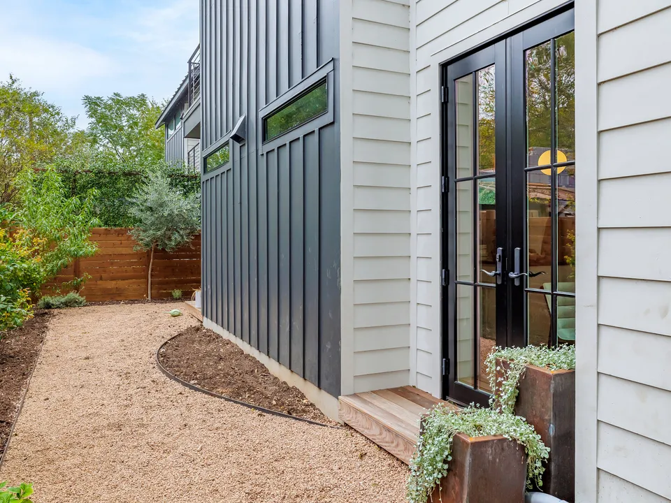 Black board and batten wall with French doors onto a gravel side yard