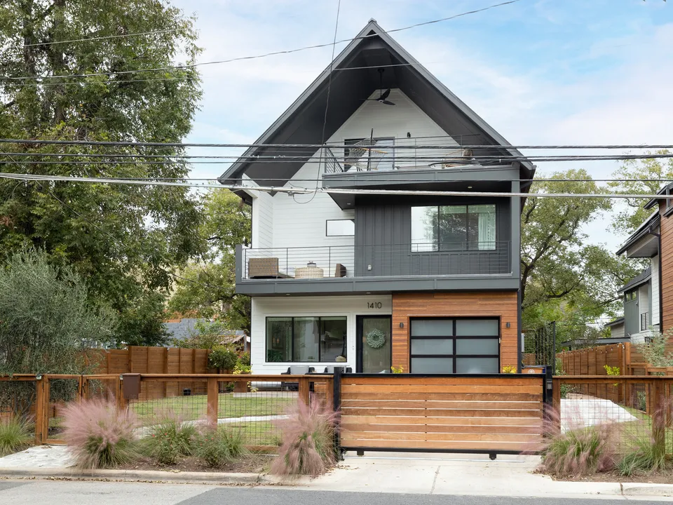 Front of the modern house behind a horizontal wood fence and ornamental grasses