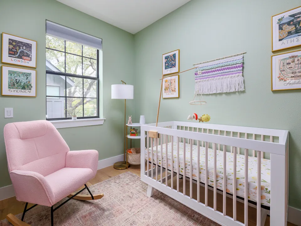 Nursery with sage walls, a white crib and a pink rocking chair