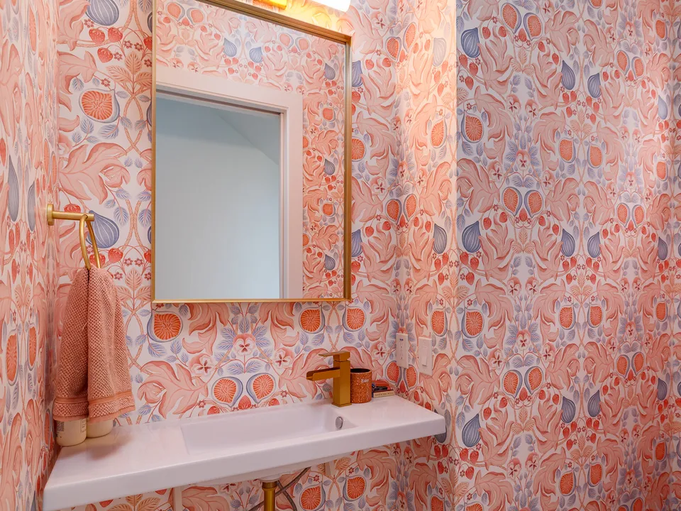 Powder bath with coral patterned wallpaper, a brass mirror and a floating sink