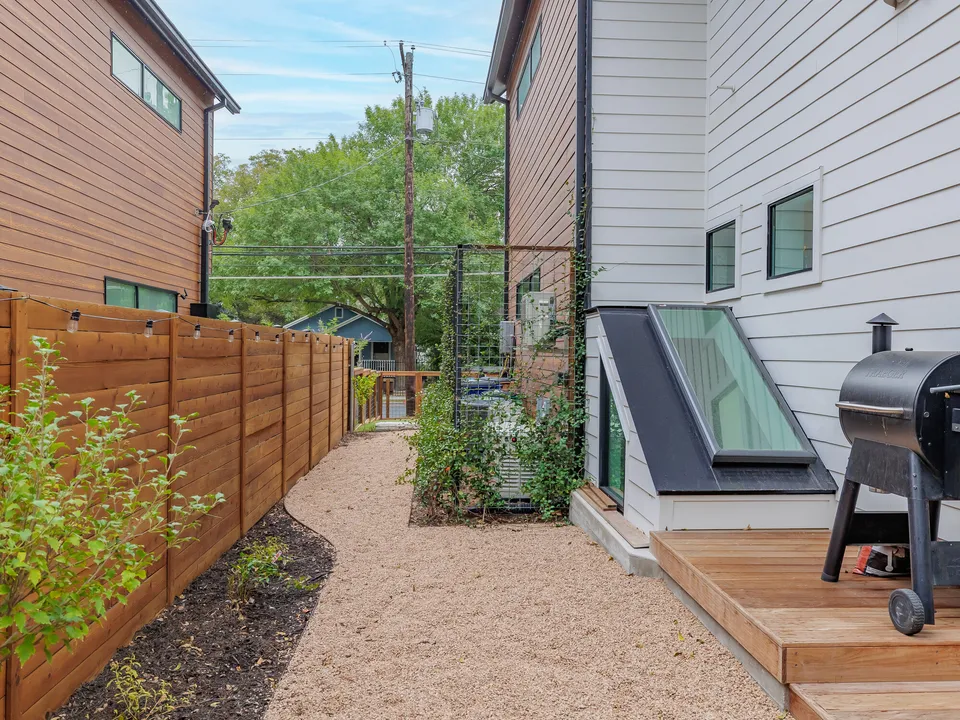 Side yard with a basement skylight, a cedar fence and a grill on a small deck