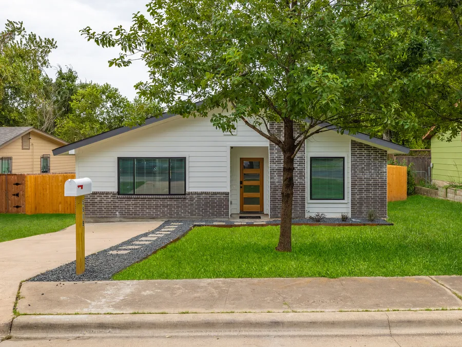 Single-story home with white siding, grey brick, and a wood front door behind a new front walk