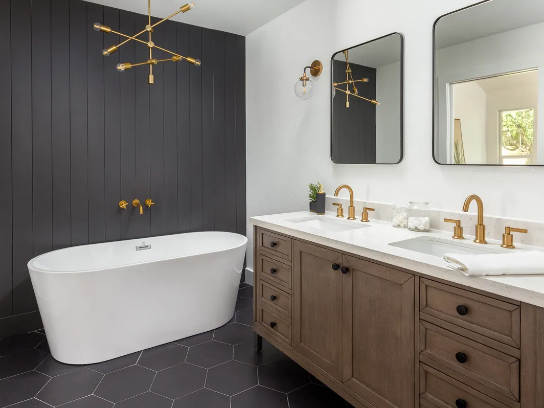 Freestanding tub against a charcoal shiplap wall beside a wood double vanity