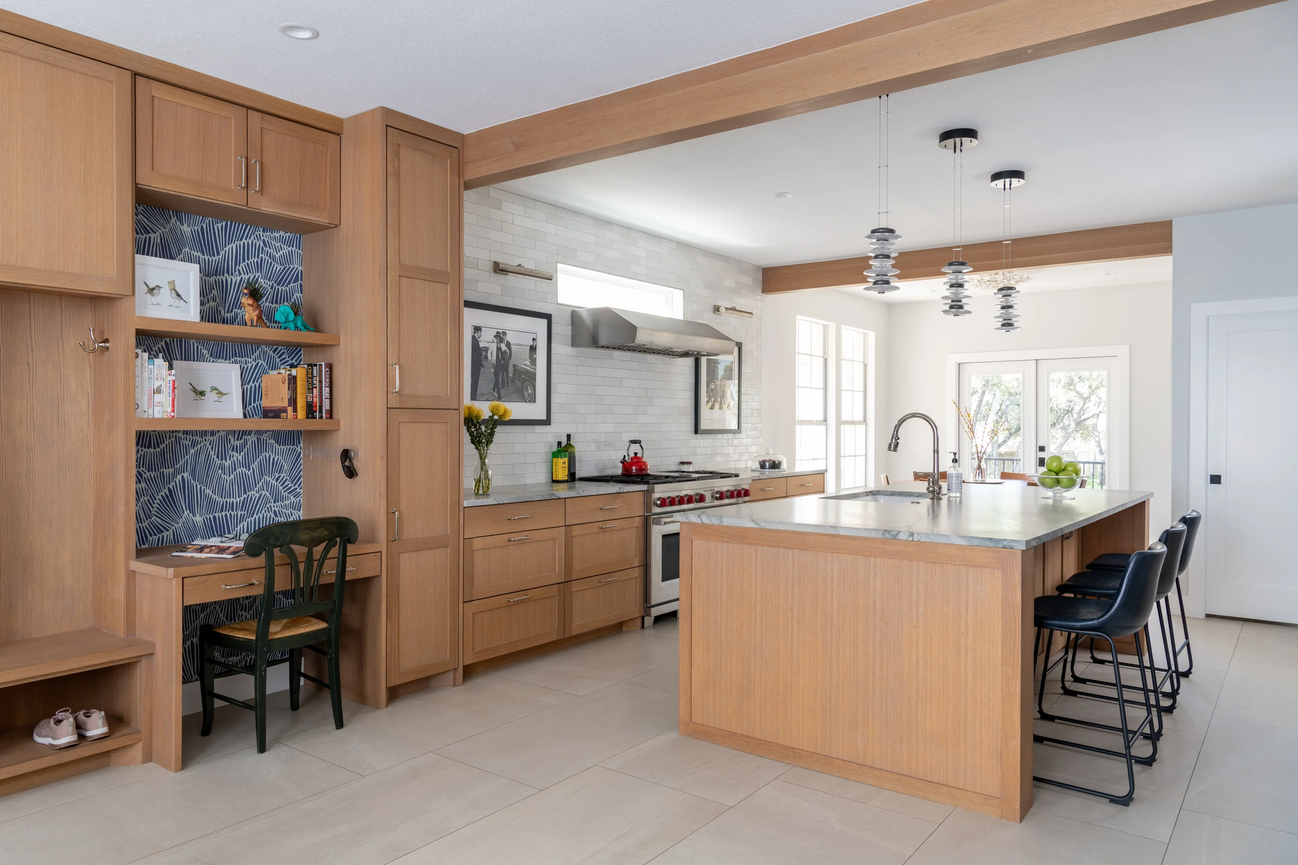 Open kitchen with white oak cabinetry, a built-in desk and cubbies, and an island with navy leather stools