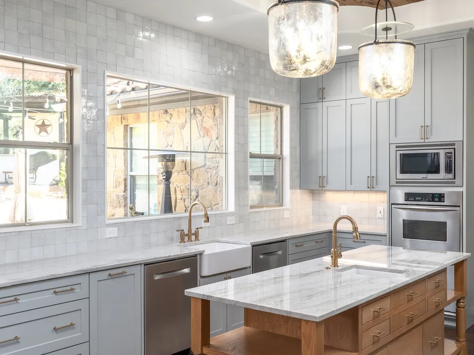 Grey cabinets and handmade tile around a farmhouse sink, with a stain-grade island
