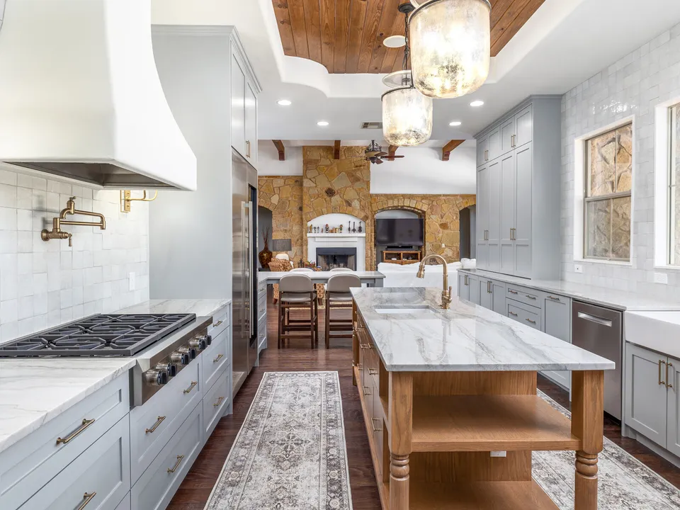 Grey cabinets and a stain-grade island with a marble top under a wood plank ceiling