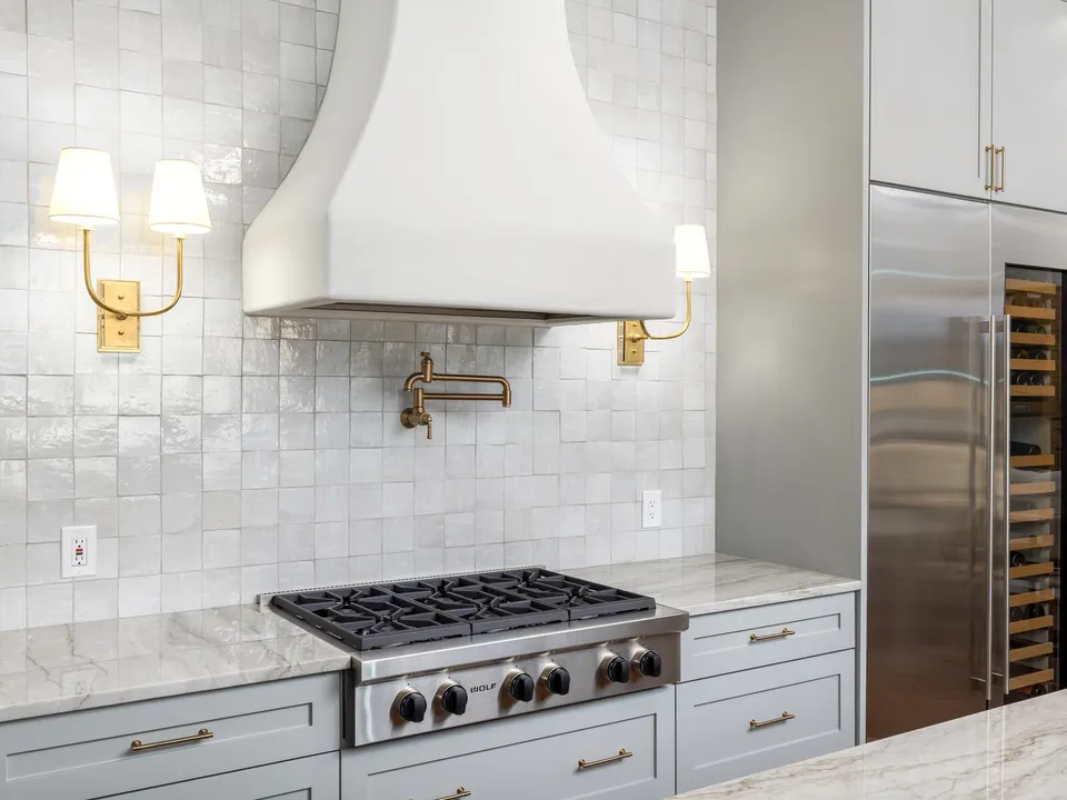 Range with a white plaster hood, a brass pot filler and brass sconces on handmade white tile