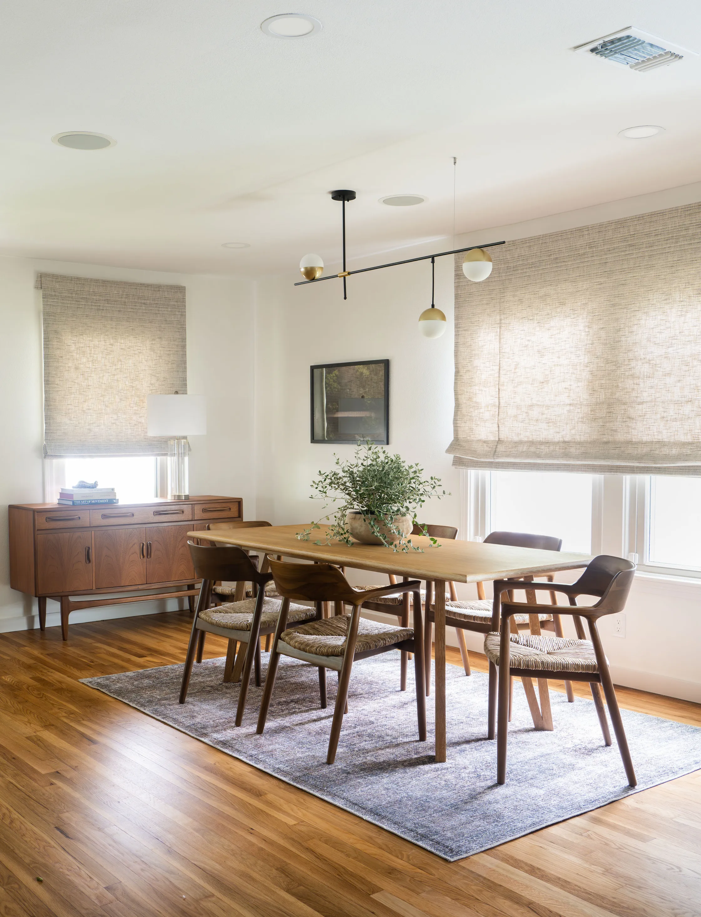 Dining room with a wood table, mid-century chairs, a walnut sideboard and woven window shades
