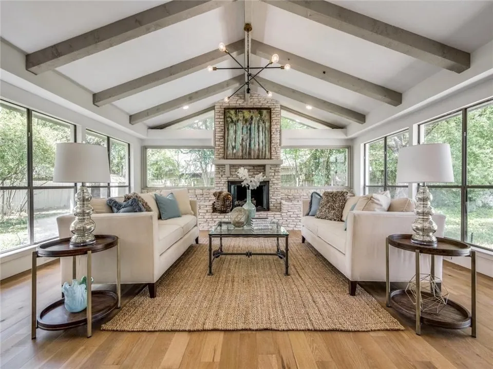 Living room with a vaulted beamed ceiling, a brick fireplace, two cream sofas and walls of windows