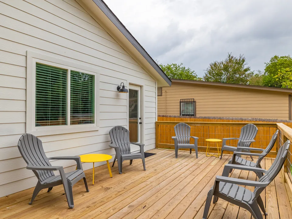 Back deck with grey Adirondack chairs, a yellow table and a cedar fence