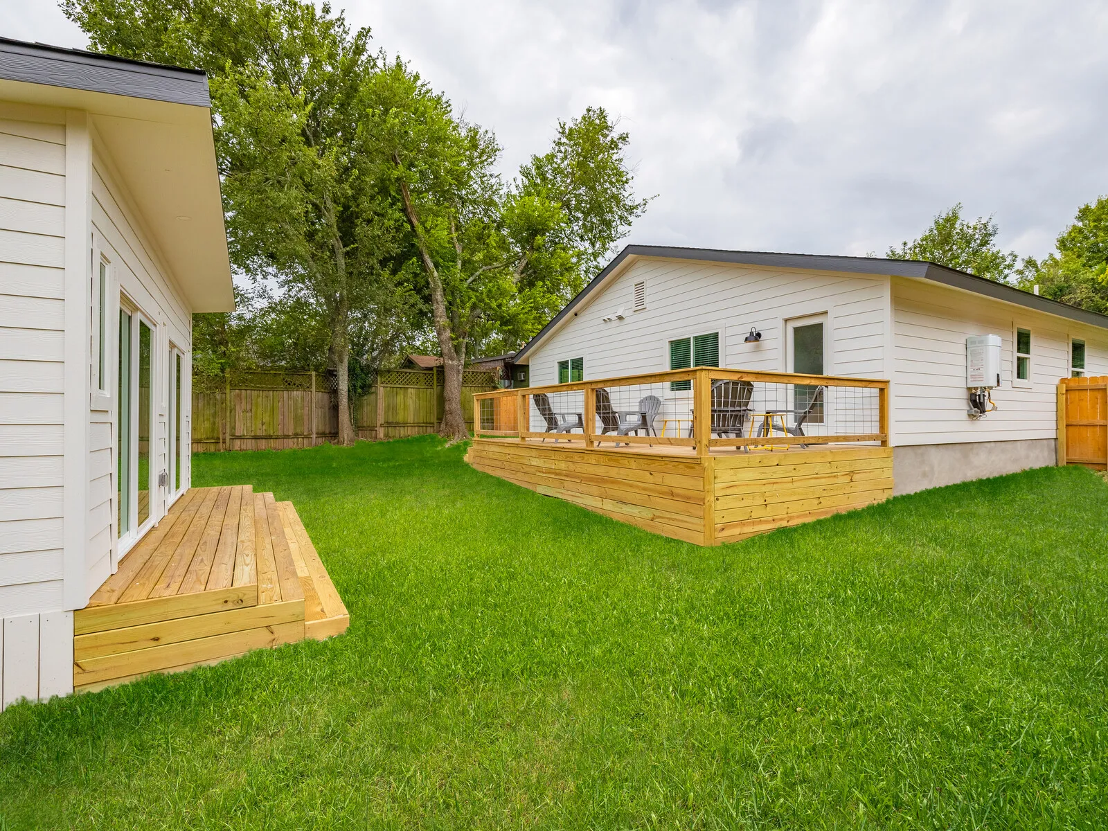 Back of a white-sided house with a new wood deck and wide steps down to the lawn