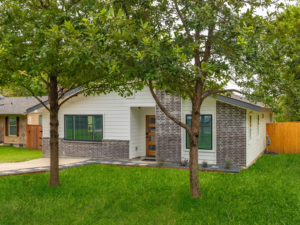 Front of the house with white siding and grey brick behind two trees