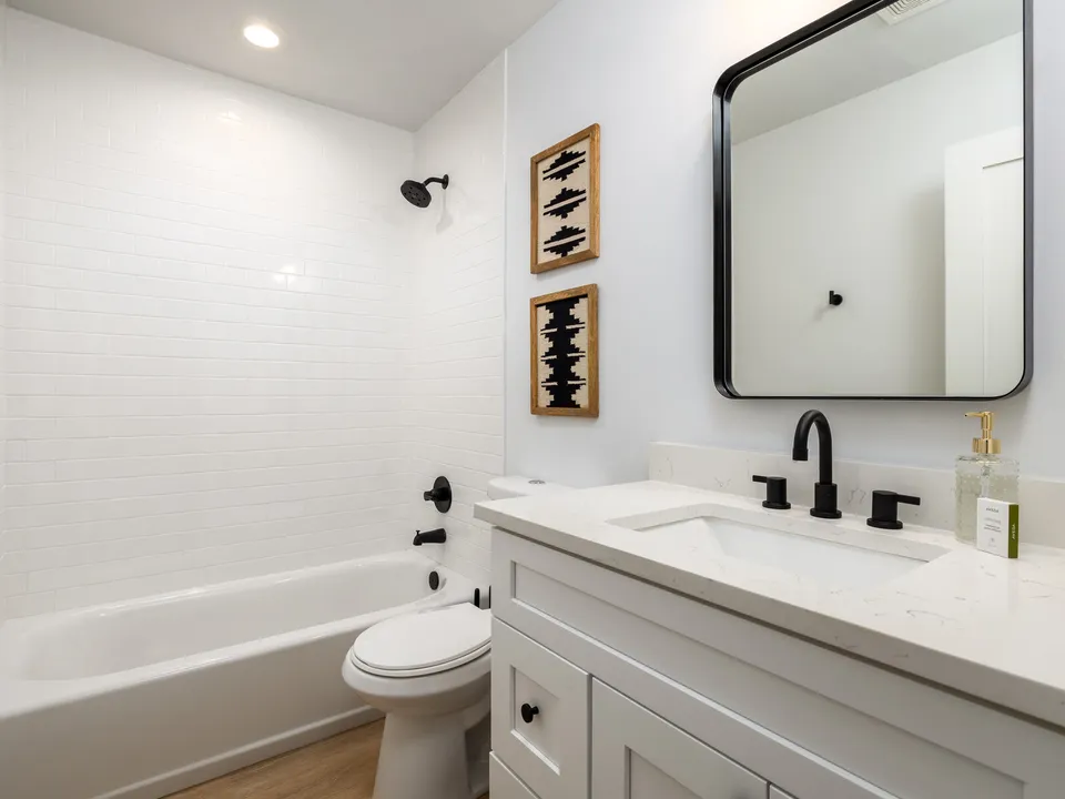 Hall bath with a white shaker vanity, a black mirror and a tub with subway tile