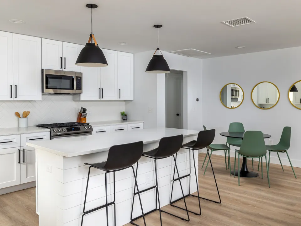 Kitchen island with black bar stools, open to a dining table with green chairs