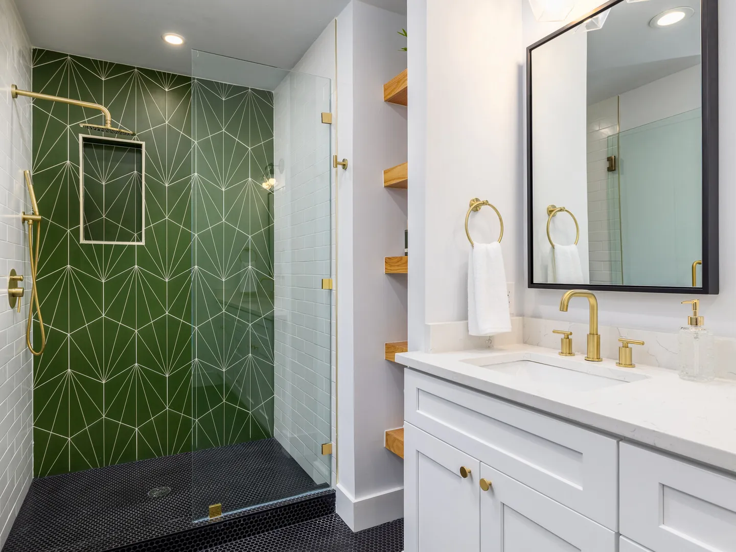 Shower with green geometric tile, black penny round floor and brass fixtures