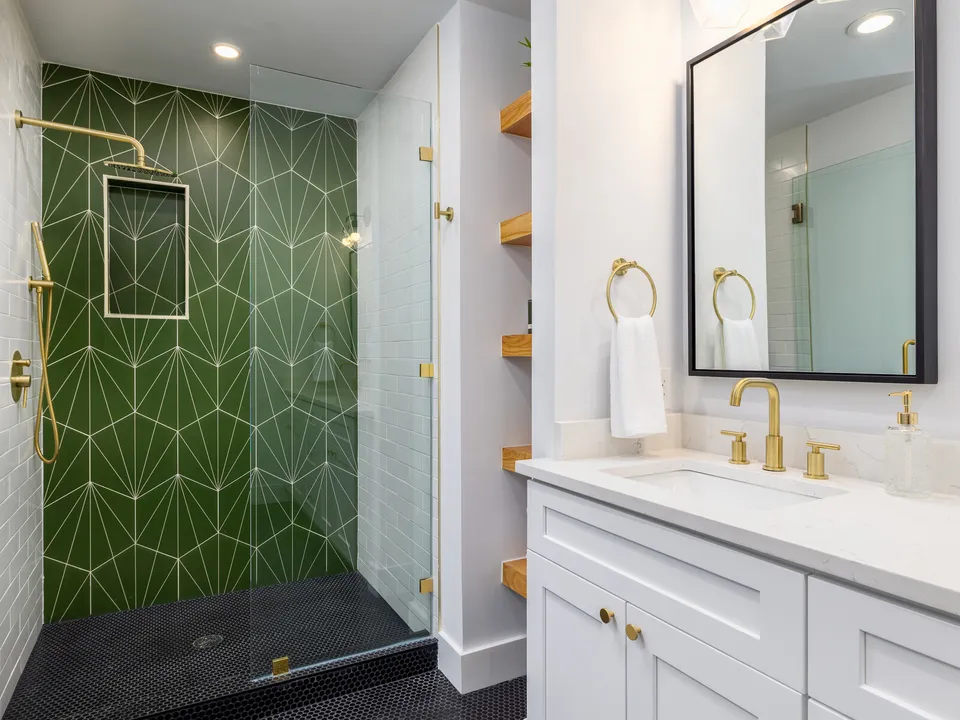 Shower with green geometric tile, black penny round floor and brass fixtures