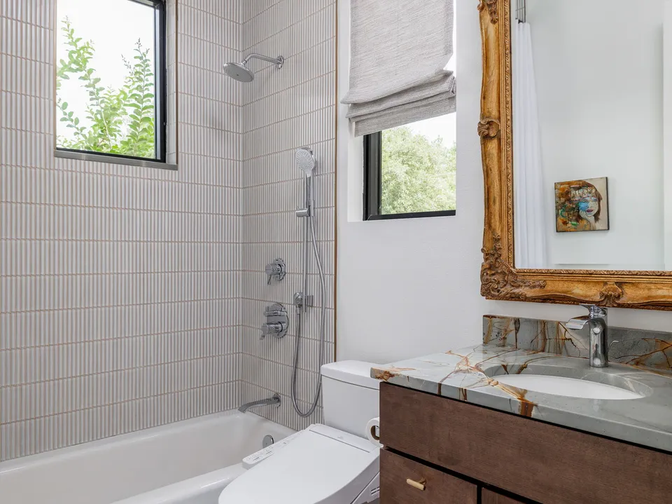 Bathroom with vertical stacked tile, a tub, a gold-framed mirror and a dark wood vanity