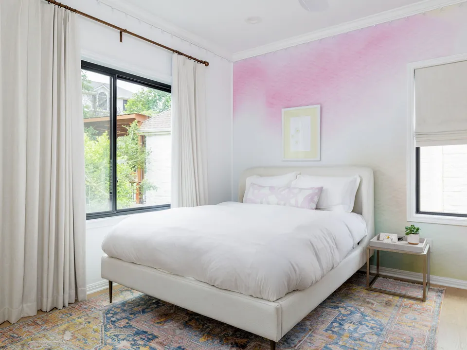 Bedroom with a pink watercolor accent wall and an upholstered white bed