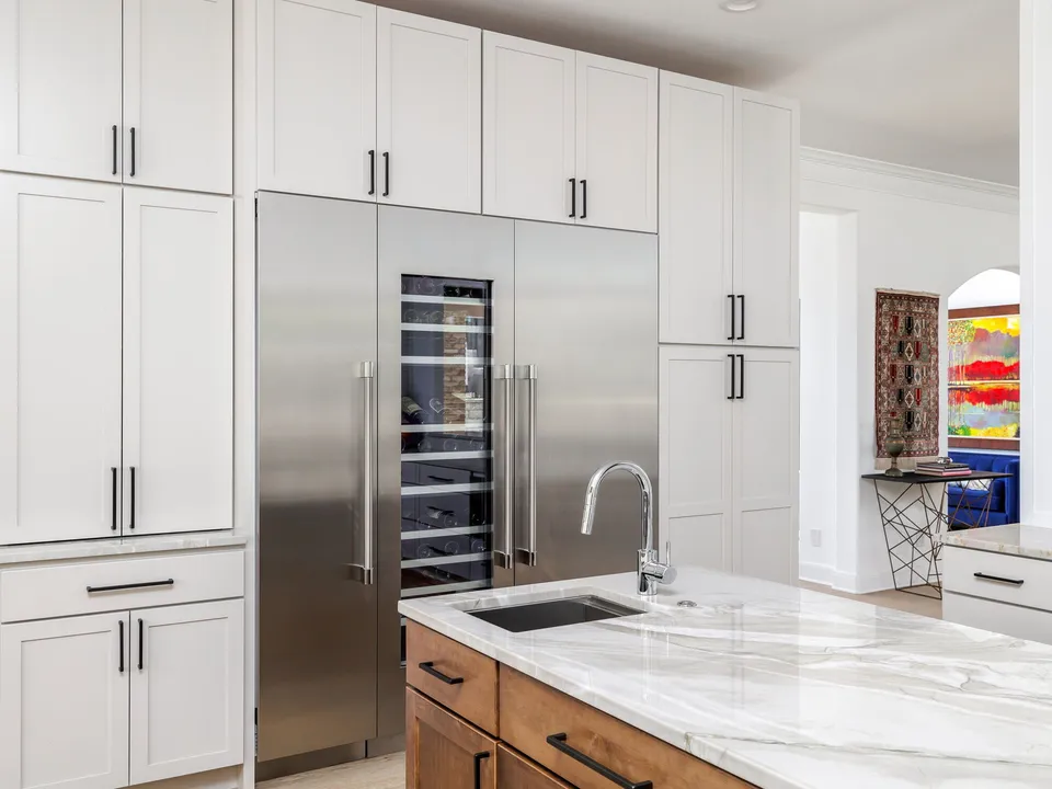 Built-in stainless refrigerator and wine column in white cabinets beside a marble island
