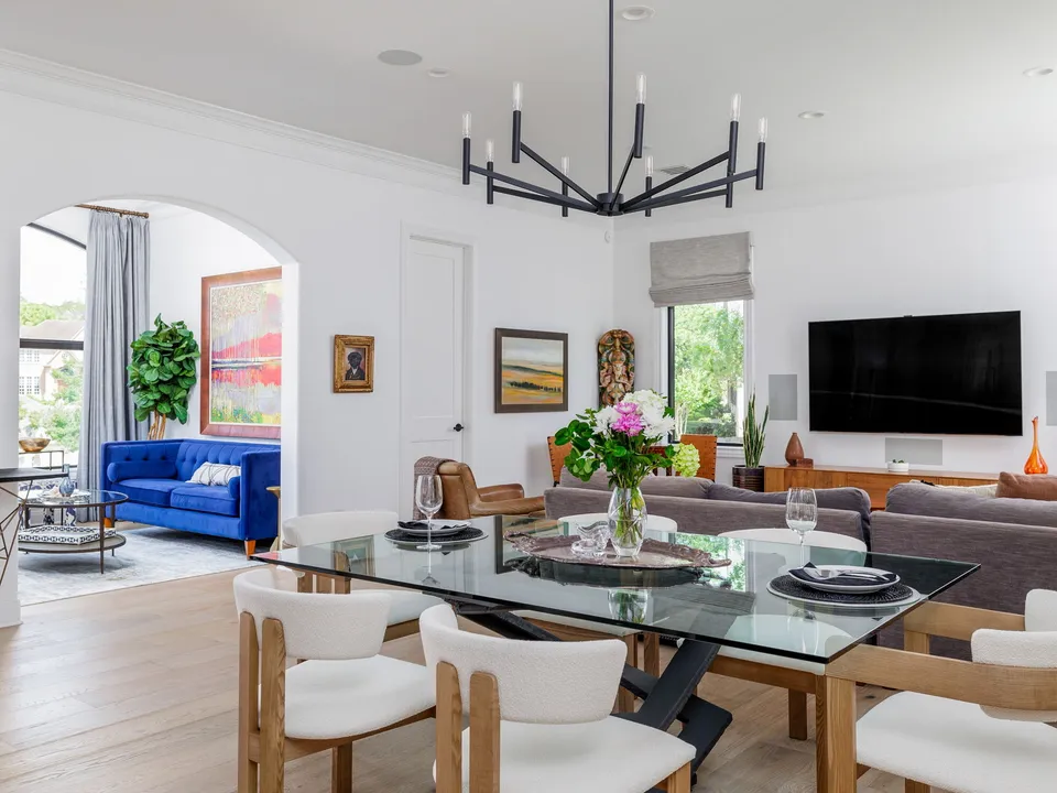 Dining room with a glass table and an iron chandelier, open to the living room