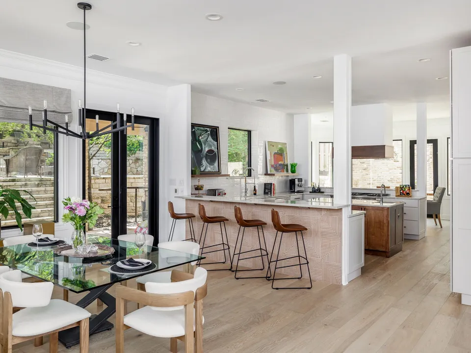 Dining table with a glass top, open to a kitchen with leather bar stools