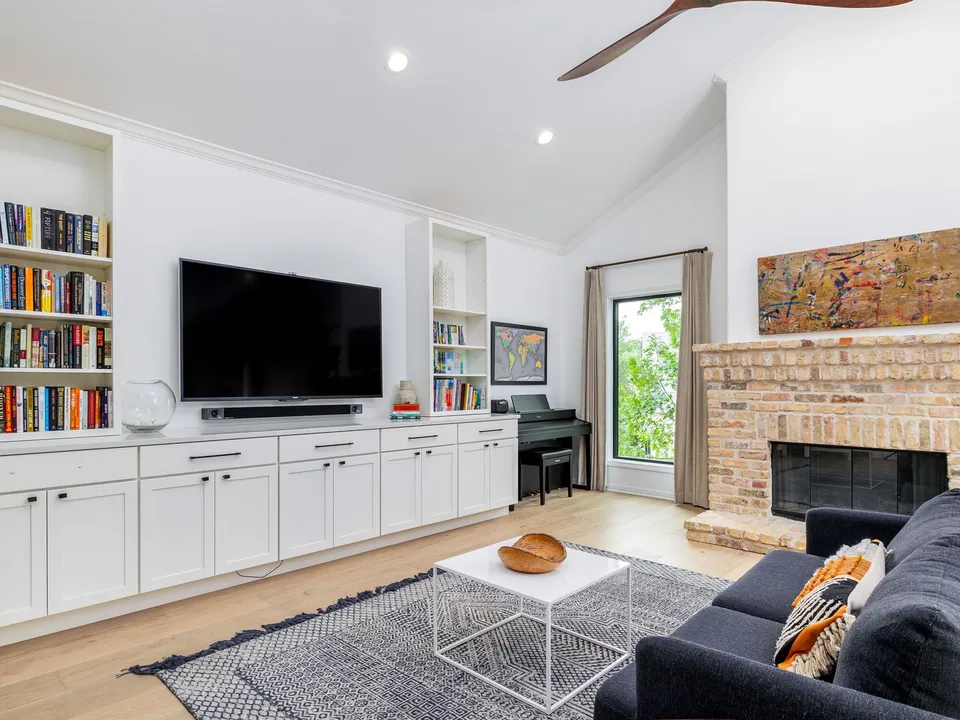 Family room with white built-ins, a TV and a brick fireplace under a vaulted ceiling