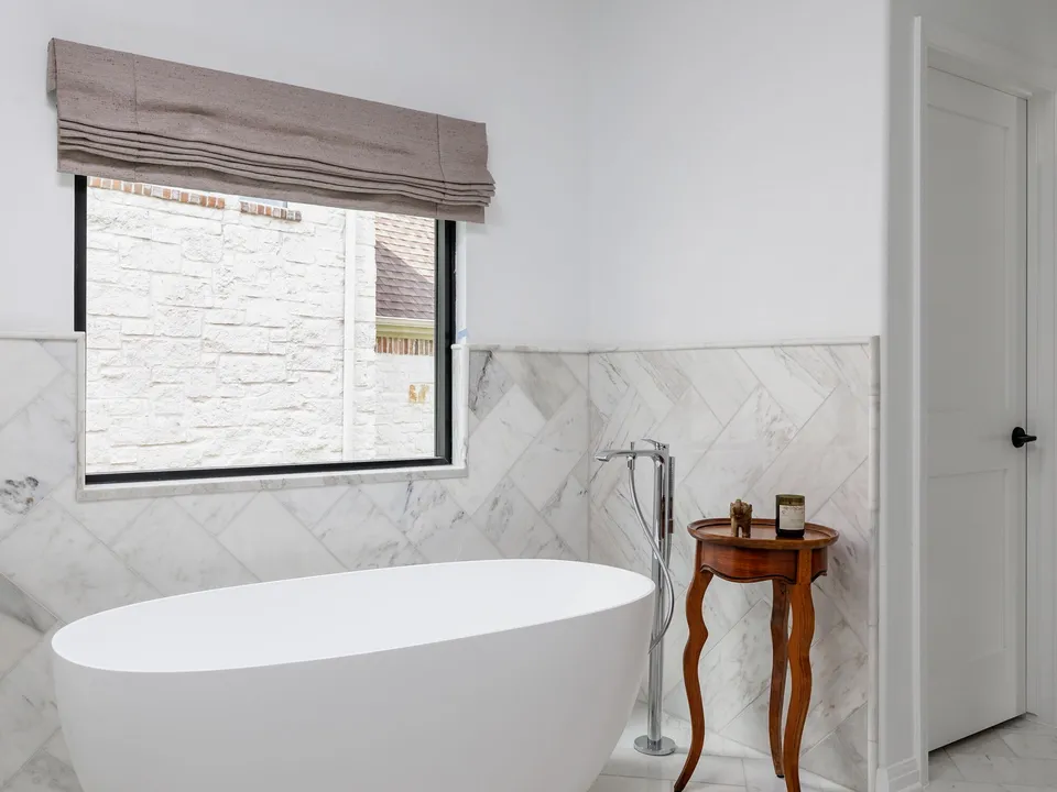 Freestanding tub below a window with marble herringbone tile