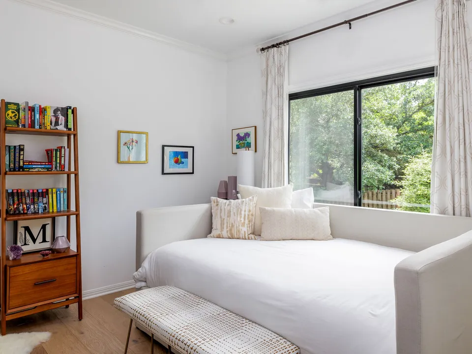Guest room with a white daybed below a window and a wood bookshelf