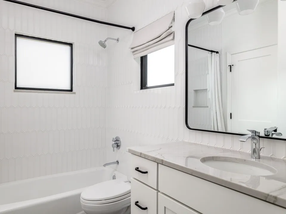 Hall bath with white stacked tile, a tub, a black-framed mirror and a marble counter