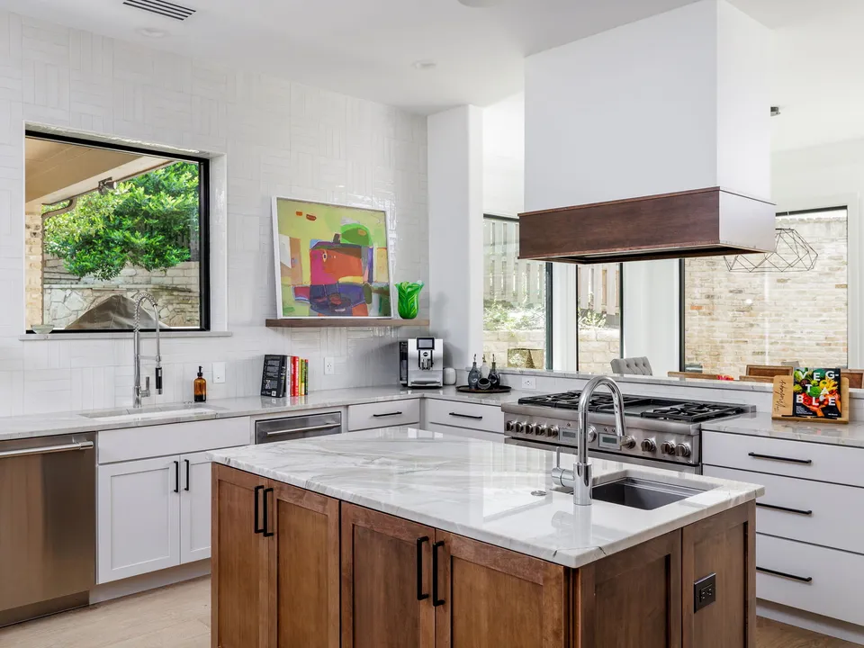 Kitchen with a wood island, a marble top, white cabinets and a wood-trimmed range hood