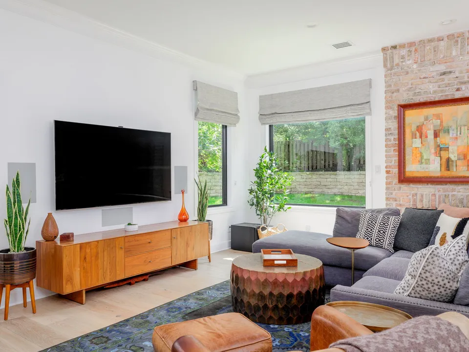 Living room with a grey sectional, a walnut media console and a painted brick wall