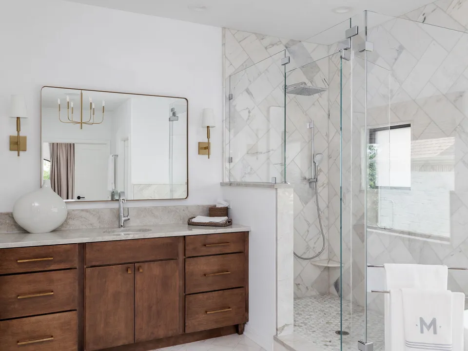 Primary bath with a wood vanity, a marble herringbone wall and a glass shower